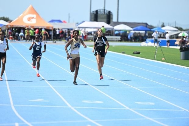 Young athletes sprint on a blue track during a track and field event, showcasing competition and sportsmanship under a clear sky.