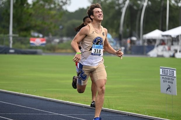 A young athlete with bib number 318 sprints joyfully on a track during a competitive event, showcasing determination and excitement.