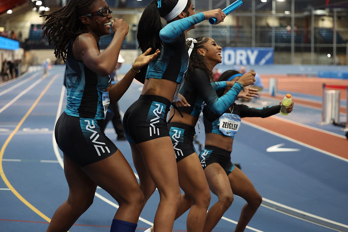 A joyful relay team celebrates after a successful race, cheering and laughing on an indoor track, showcasing teamwork and athletic spirit.