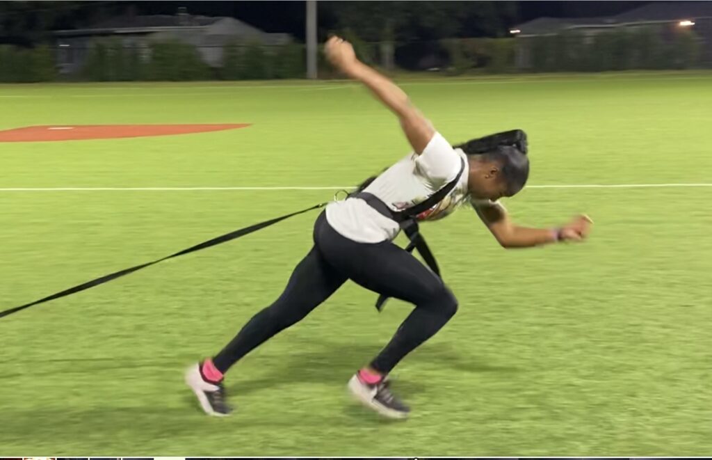 Athlete sprinting on a field while harnessed, demonstrating speed training with resistance equipment at night.