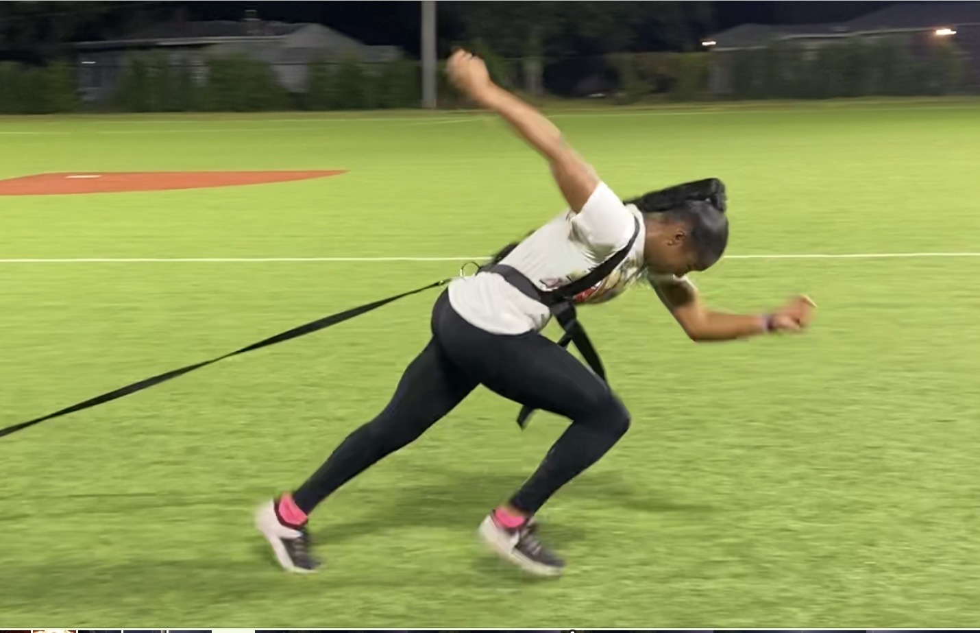 Athlete sprinting on a field while harnessed, demonstrating speed training with resistance equipment at night.