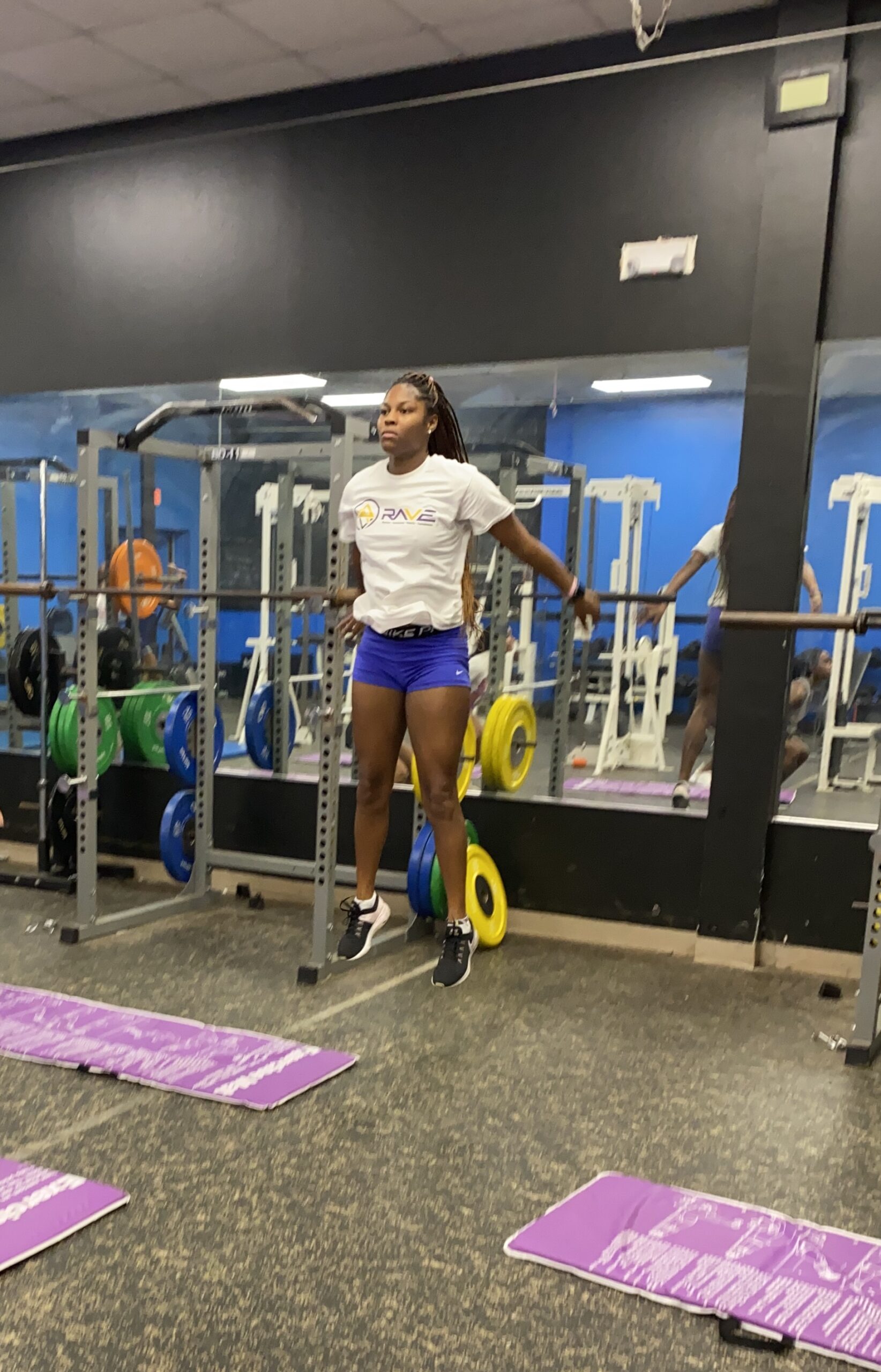 Athlete performing a jump exercise in a gym, showcasing strength and focus. Colorful weight plates and gym mats are visible in the background.