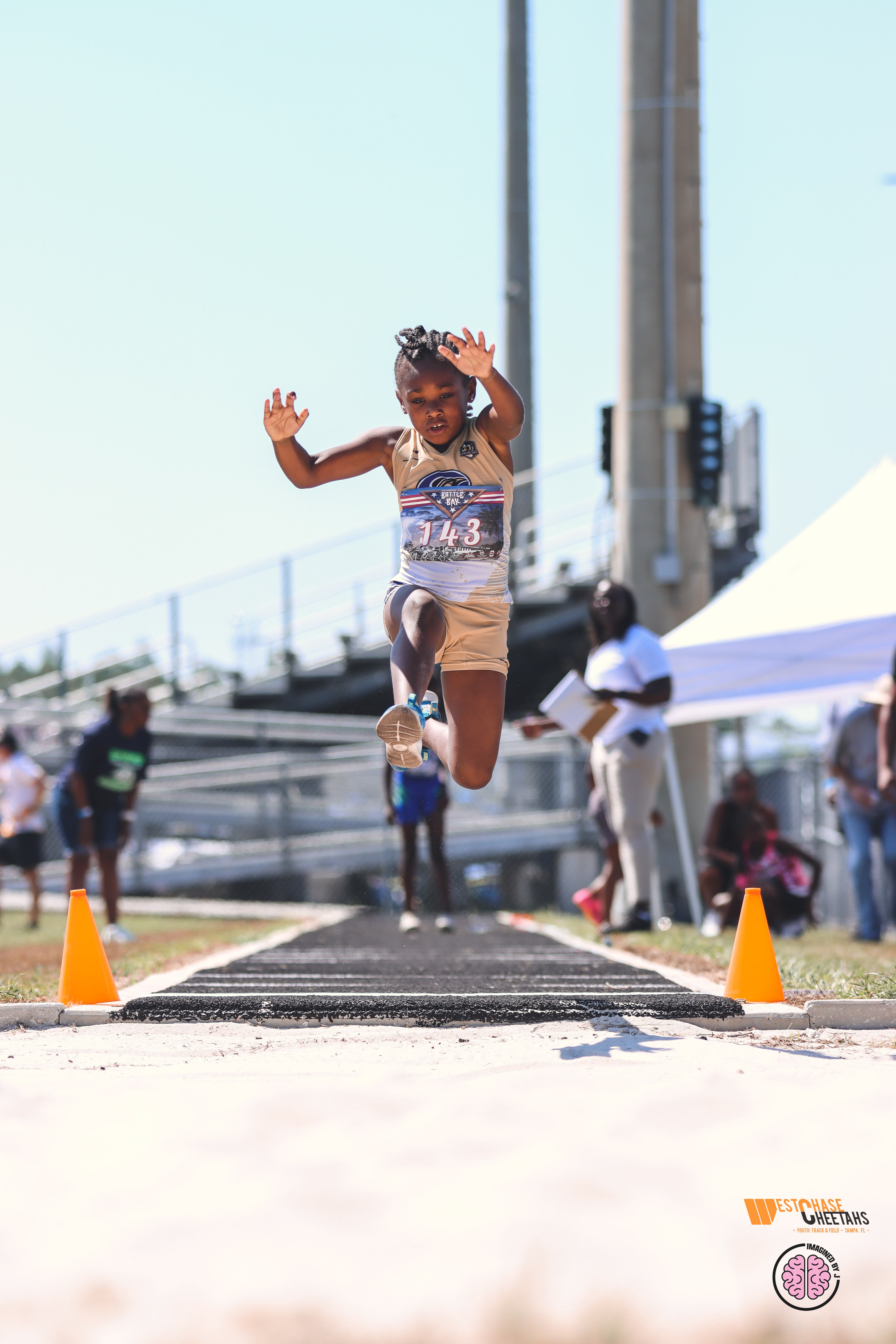 A girl in athletic wear leaps into the air during a long jump event, demonstrating focus and determination at an outdoor track meet.