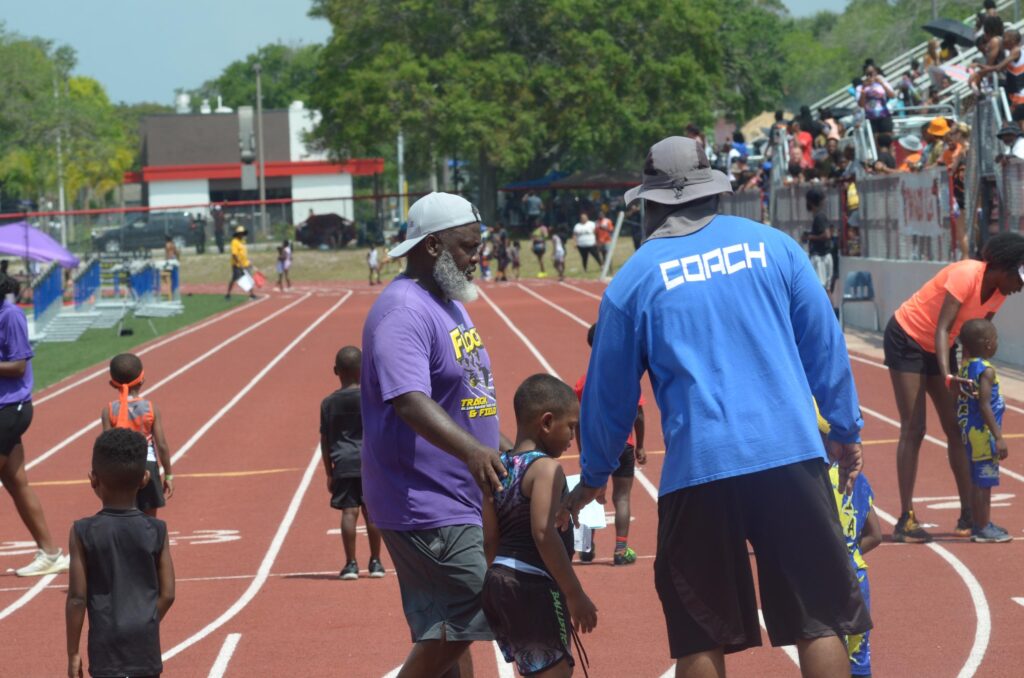 Coaches guide young athletes on a track during a youth track event, showcasing teamwork and athletic development in a competitive setting.