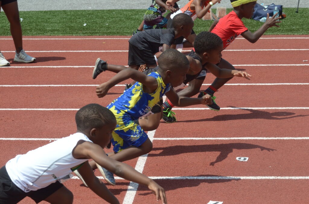 Young athletes burst off the starting blocks during a track and field event, showcasing determination and athleticism on a red rubber track.